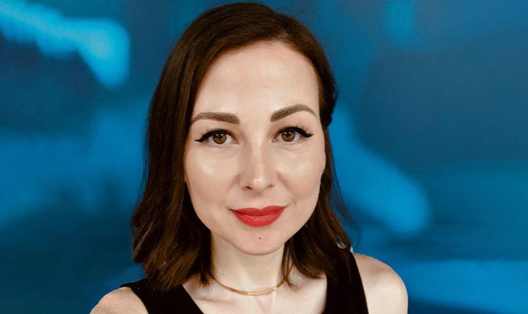 Portrait of Zeinab Hijazi with short dark-brown hair and red lipstick. She is wearing a black tank top and a gold necklace. The background is a blue and white abstract pattern.