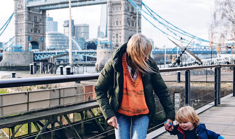Grandmother holding her grandson's hand while walking on a wooden walkway near the Tower Bridge in London, UK