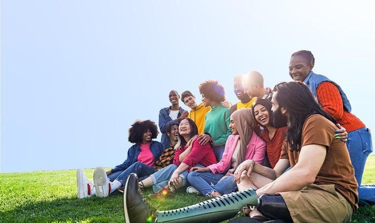 Diverse multiethnic people enjoying themselves outdoors sitting on the grass in a city park